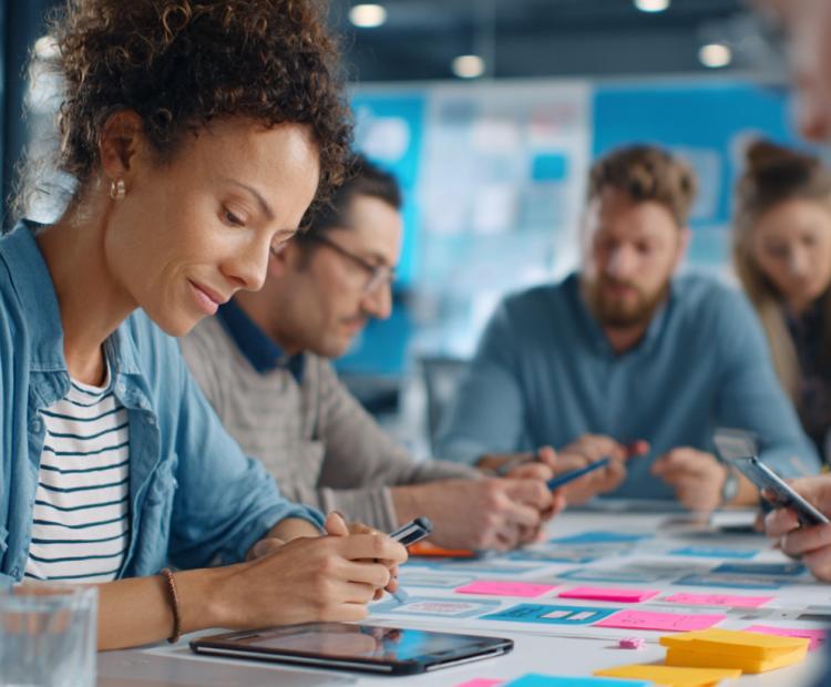 Close-up of a diverse team of learning designers and product strategists collaborating over wireframes, curriculum pages, and tablet prototypes
