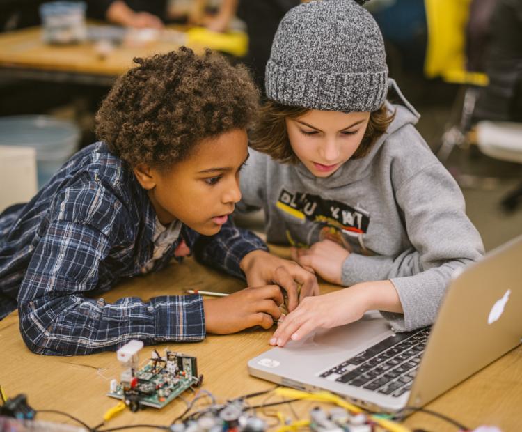 a photograph of two middle school students working on an engineering project with laptops and tools, surrounded by various electronic components like motherboards and circuit boards. they appear focused yet joyful in their creativity as they collaborate to build something innovative.